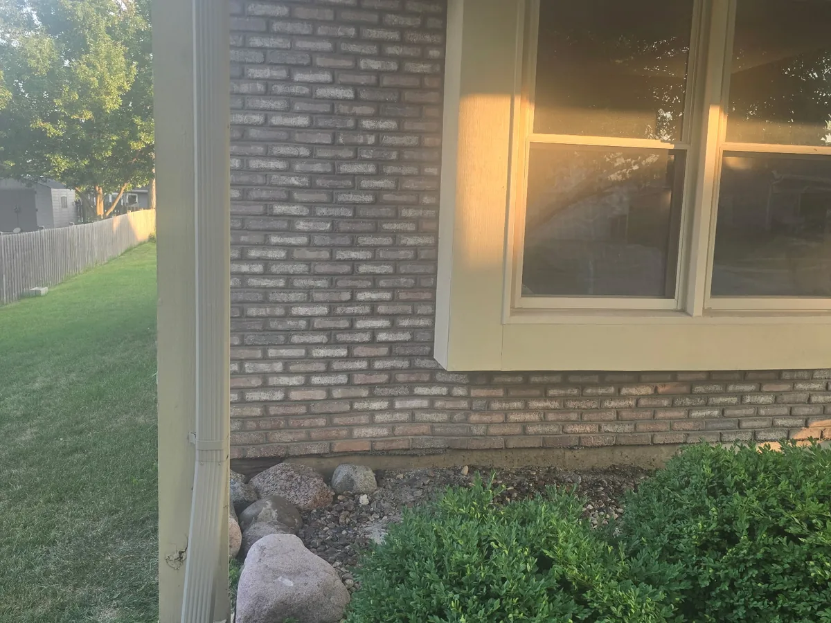 Corner of a light brick home exterior with a bay window and landscaping stone
