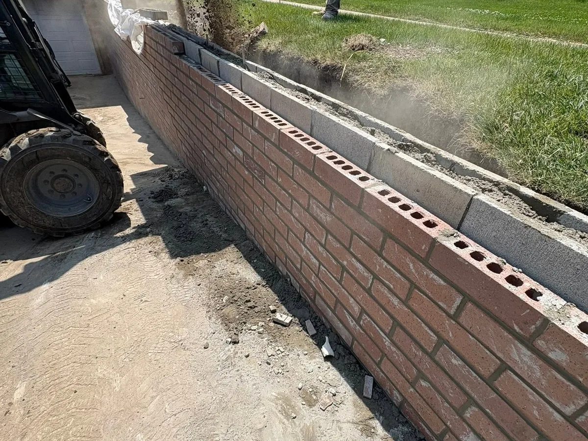 Red brick retaining wall being built along a driveway with a skid steer nearby