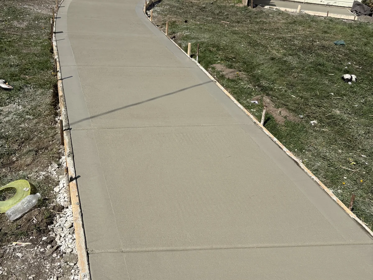 New concrete sidewalk running up a sloped yard beside stone edging