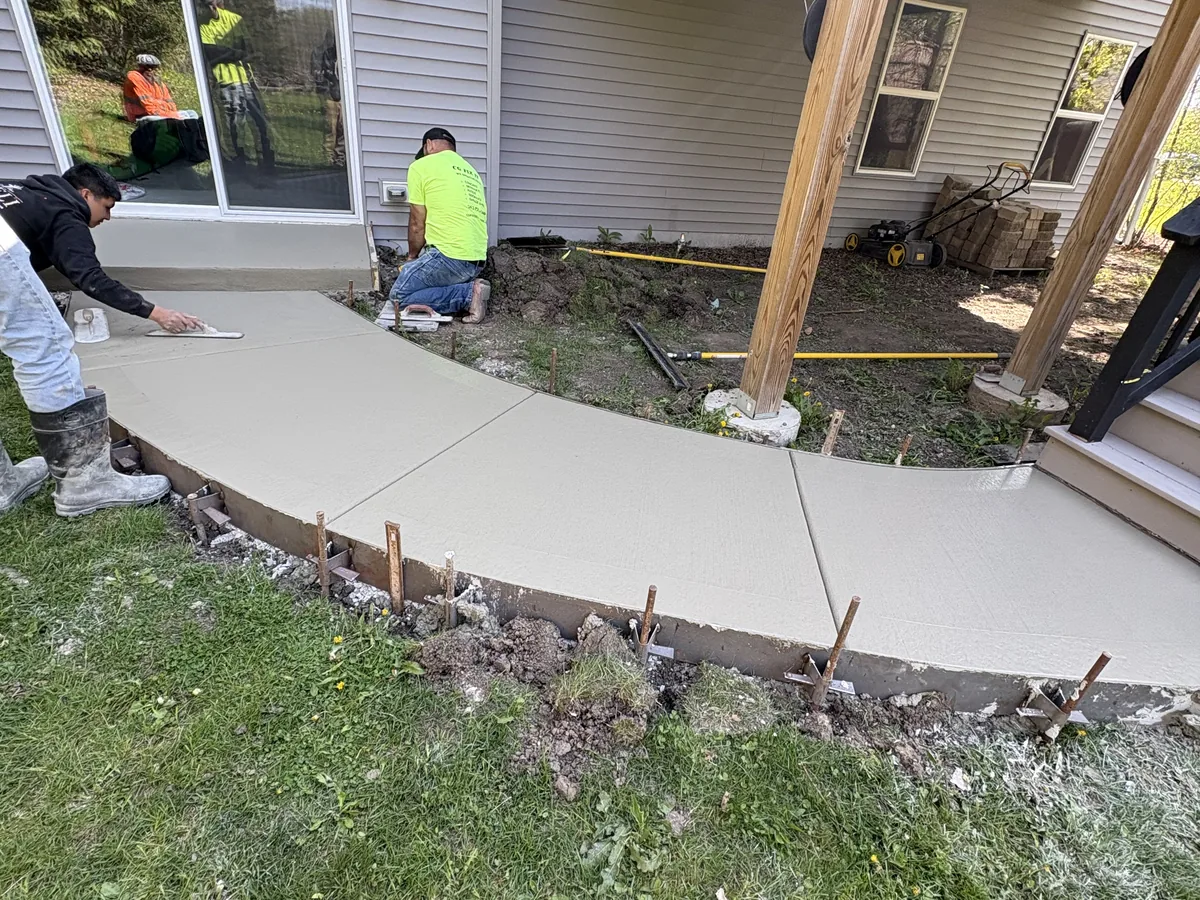 Crew troweling a curved concrete walkway alongside a house