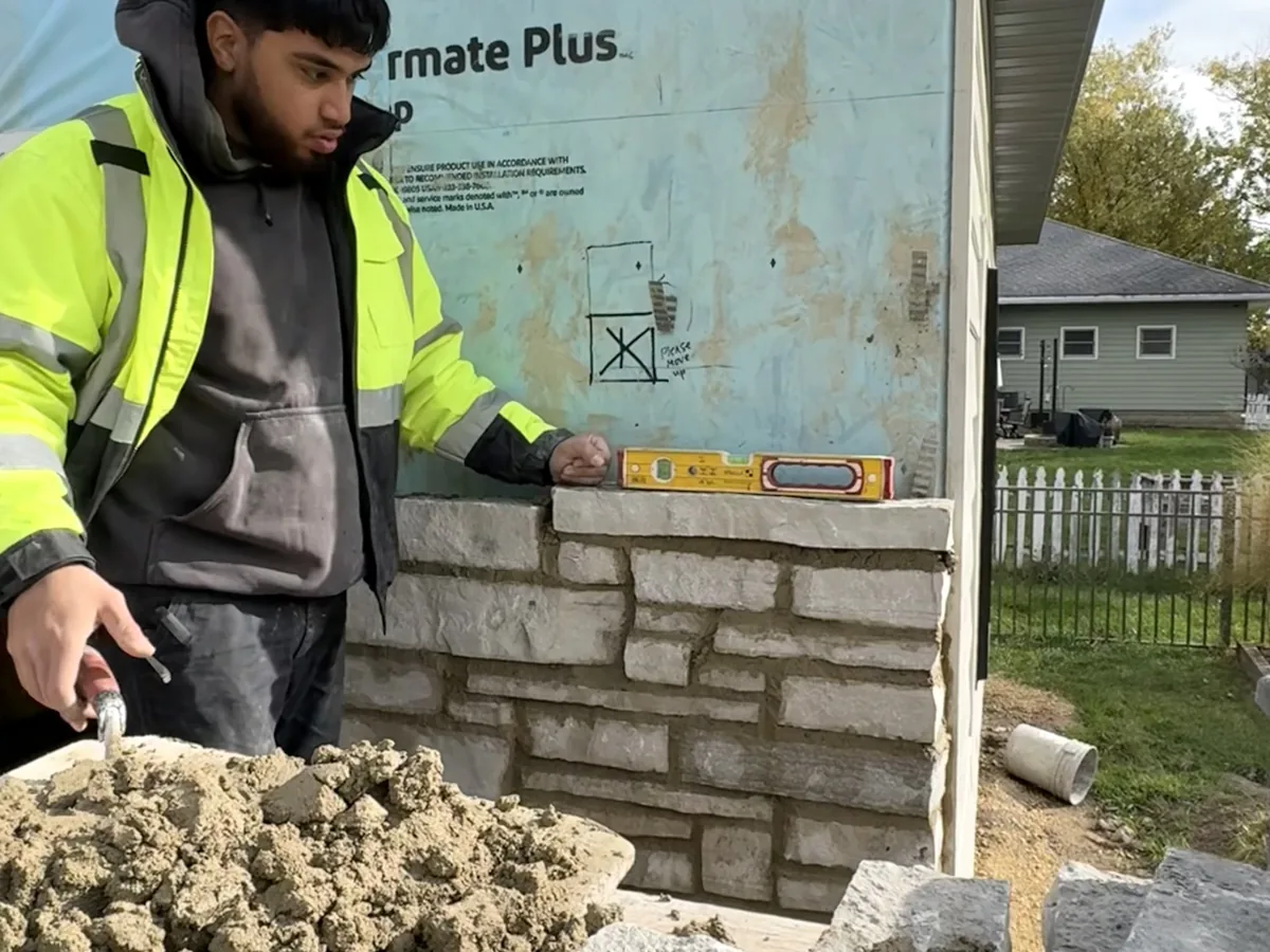 Mason checking a cut stone veneer wall with a level during installation