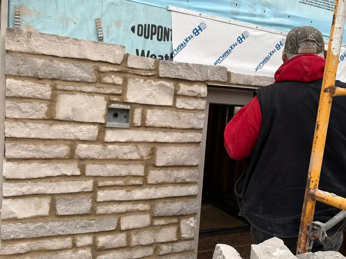 Mason setting cut stone veneer over house wrap on an exterior wall