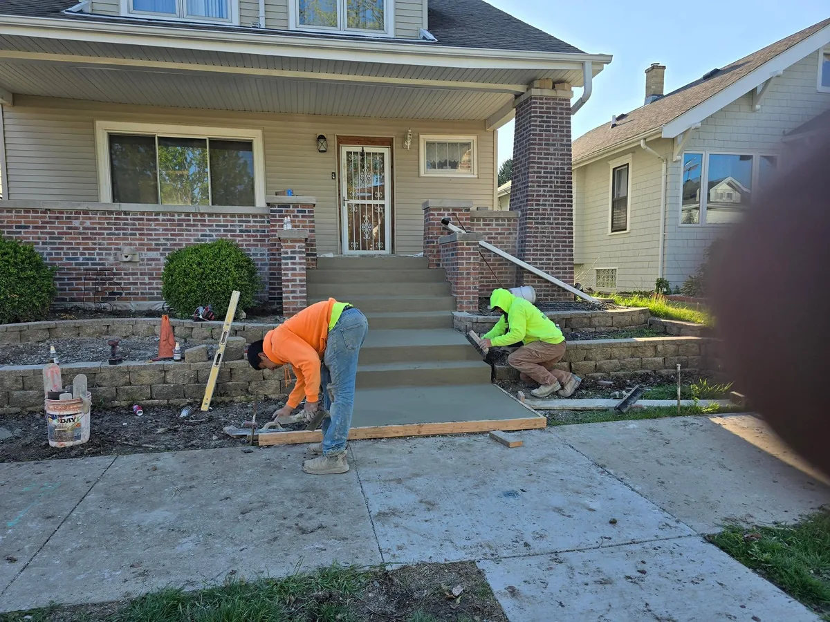 Crew finishing concrete front porch steps at a brick home
