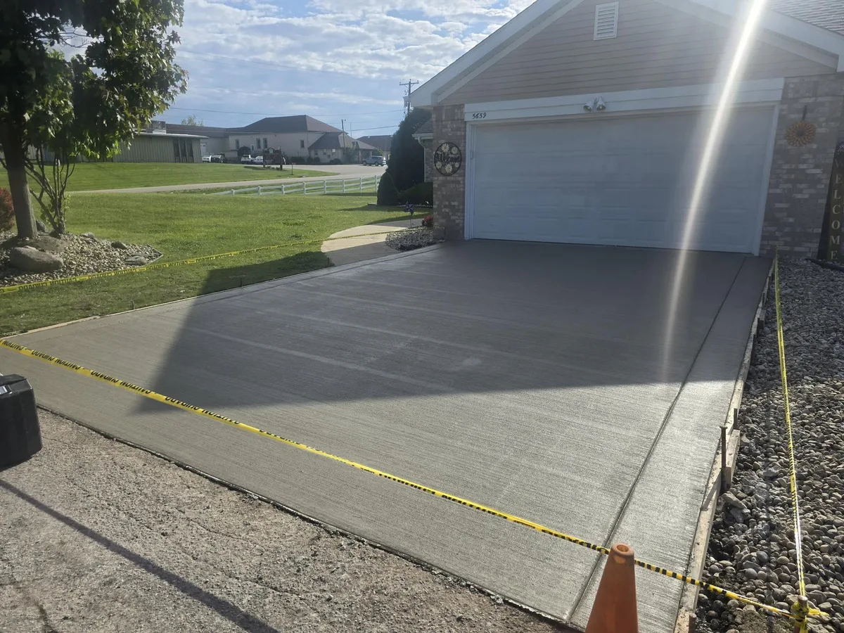 Freshly poured concrete driveway marked off with caution tape in front of a garage