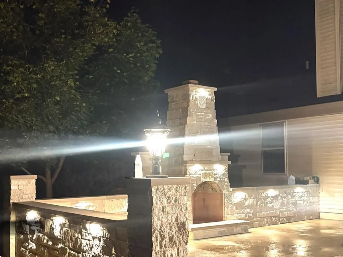 Custom outdoor kitchen with a cut stone fireplace and chimney lit up at night